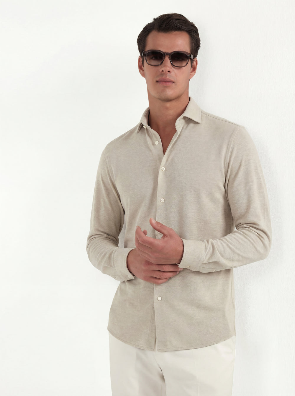 Man wearing a light beige button-up shirt and sunglasses on a white background