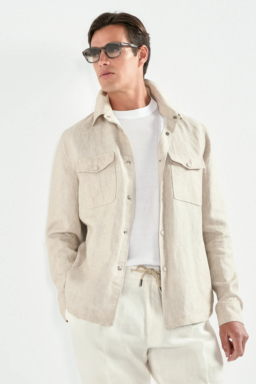 Man wearing a beige jacket, white shirt, and pants against a white background