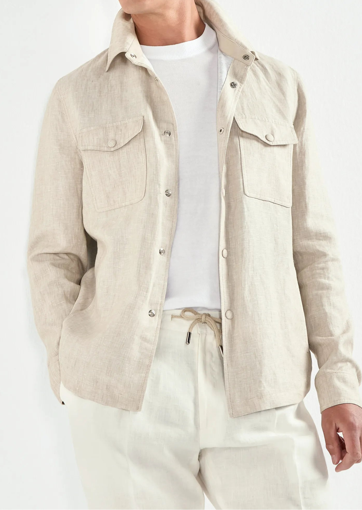 Man wearing a beige jacket, white shirt, and pants against a white background