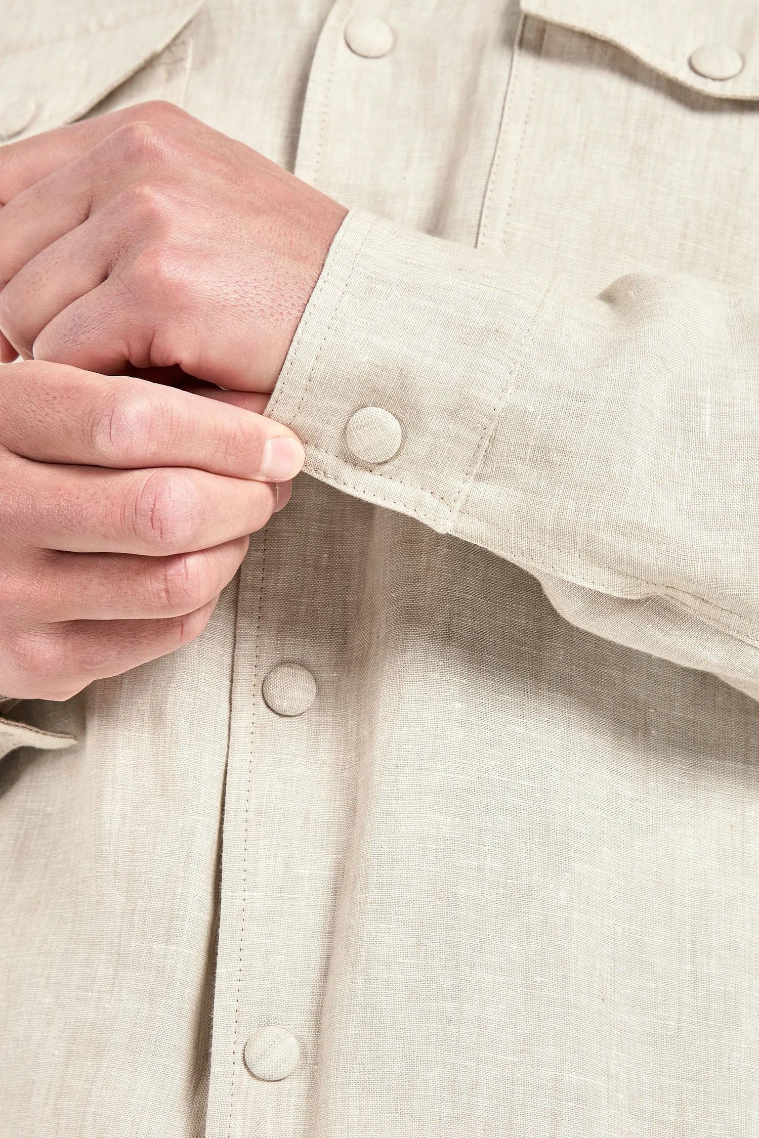 Close-up of a beige shirt with buttons and a hand adjusting the sleeve.