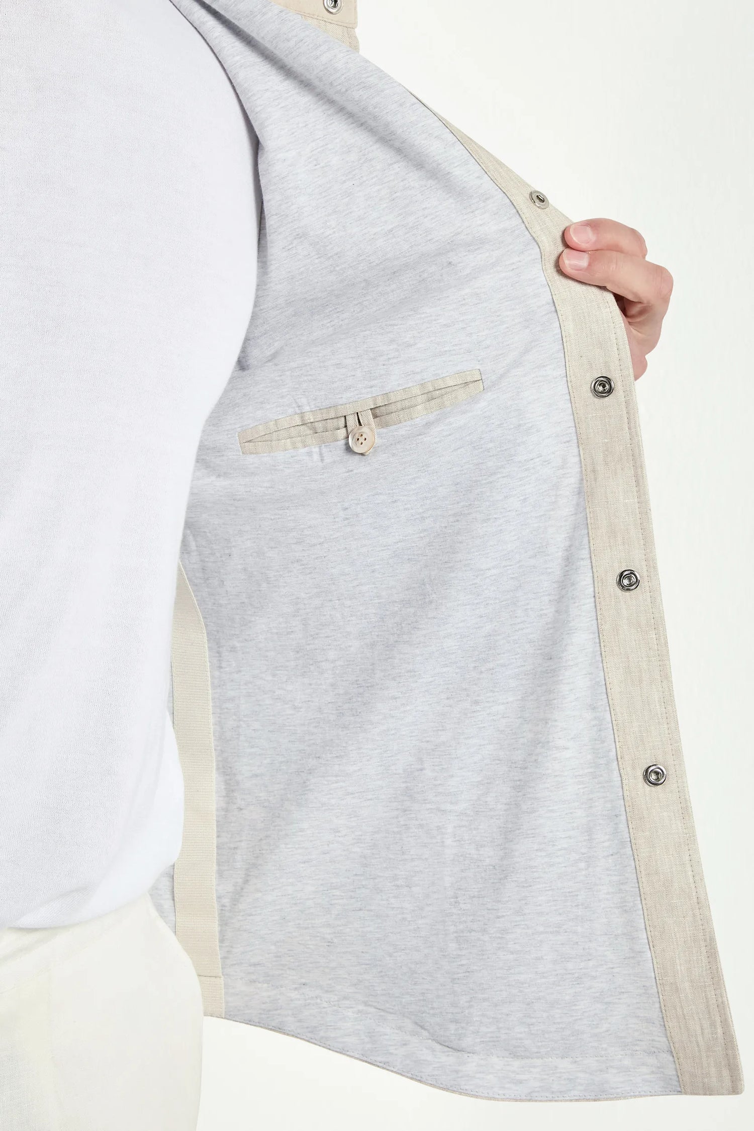 Gray jacket with beige trim held open by a hand on a white background