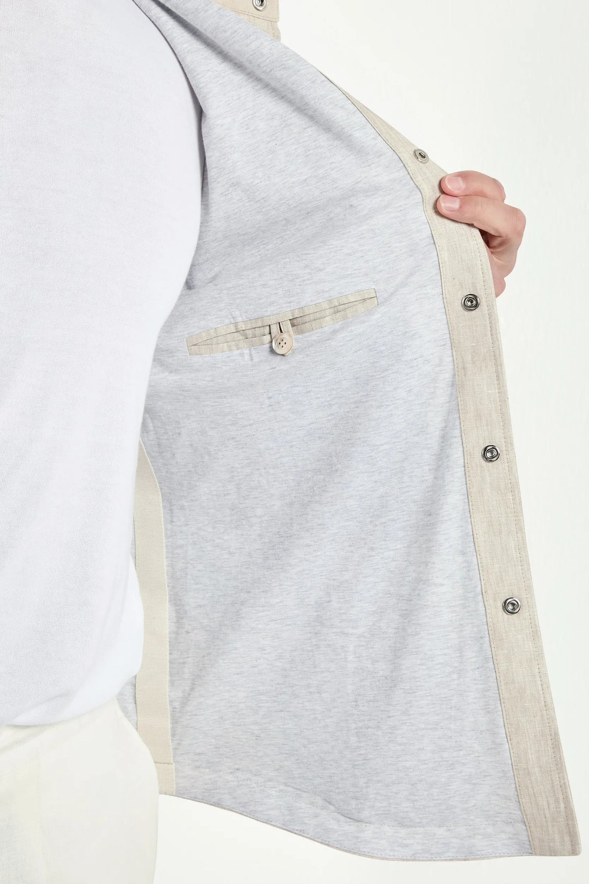 Gray jacket with beige trim held open by a hand on a white background