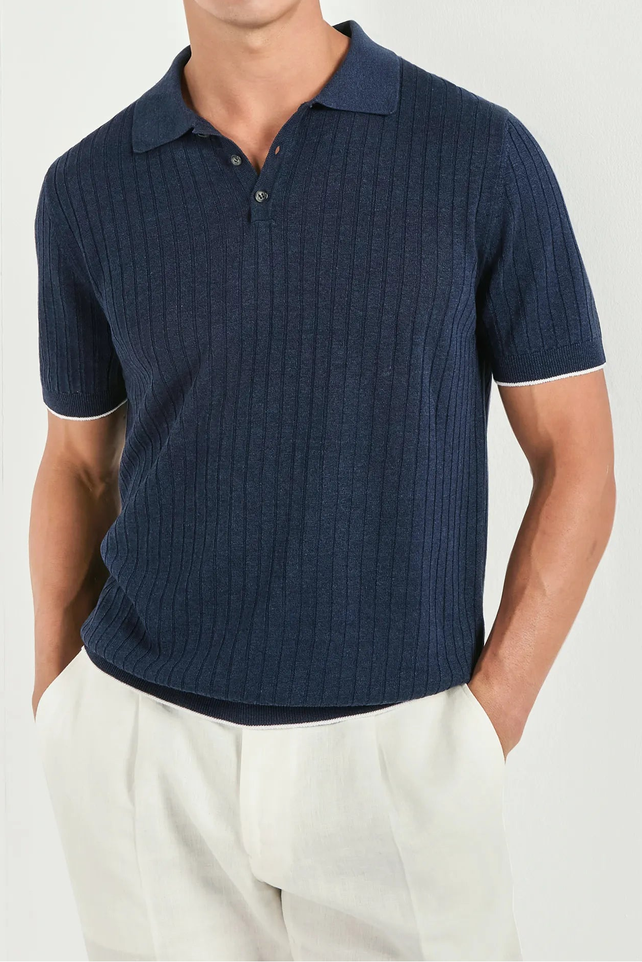 Man wearing a navy ribbed polo shirt and sunglasses on a white background