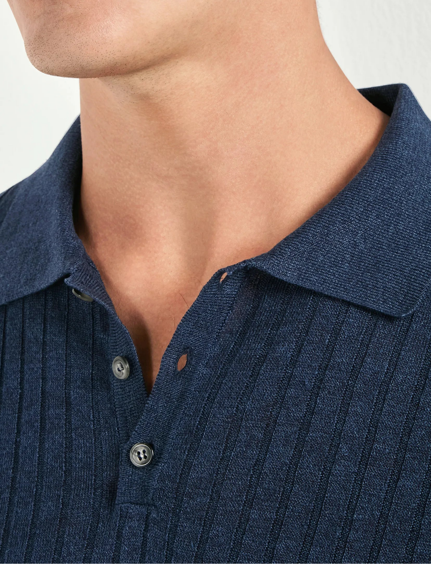 Close-up of a person wearing a blue ribbed polo shirt against a neutral background