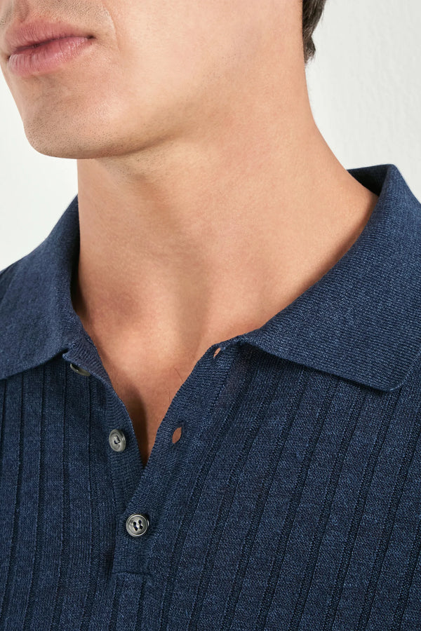 Close-up of a person wearing a blue ribbed polo shirt against a neutral background