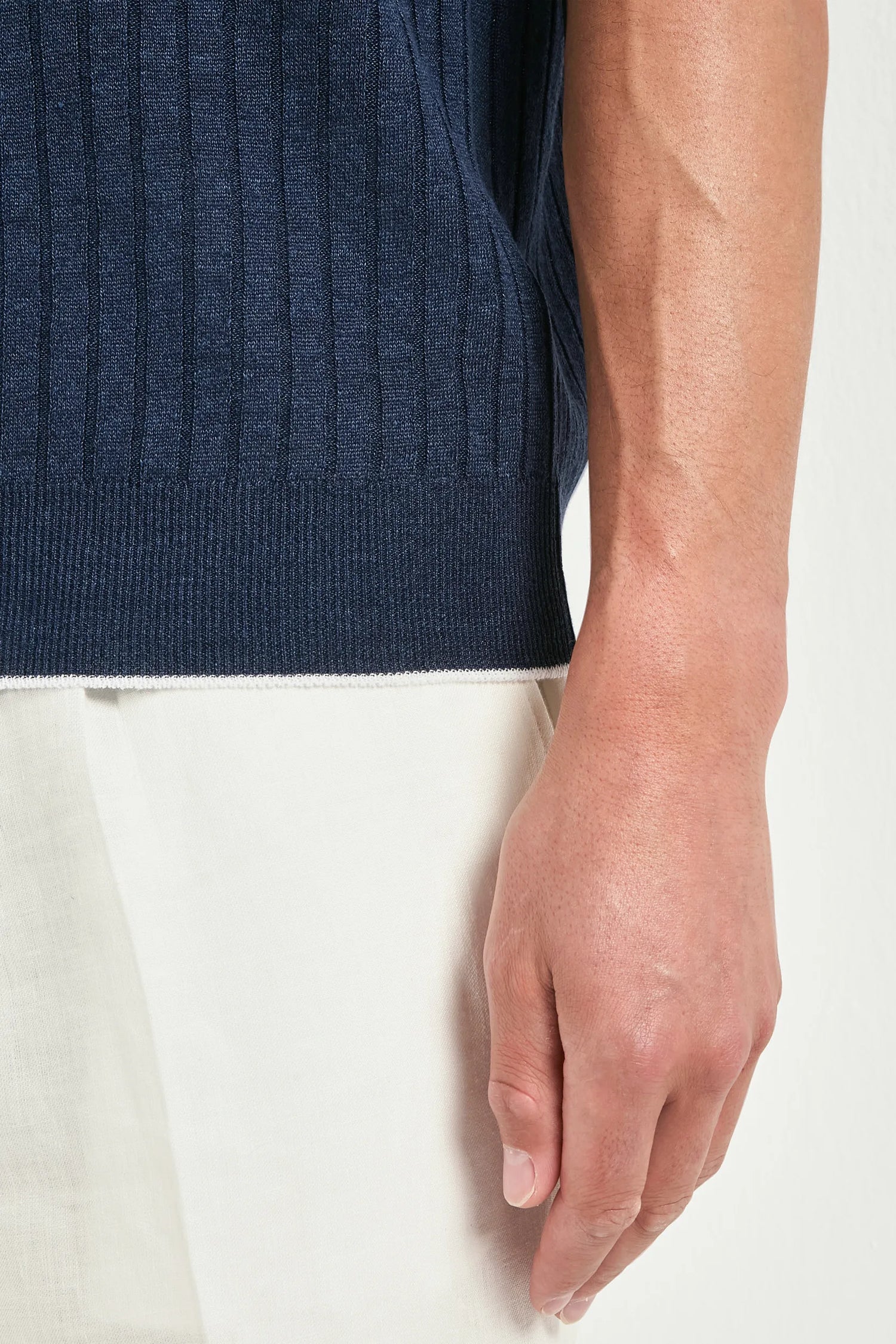 Close-up of a person wearing a navy blue sleeveless sweater and white pants on a white background