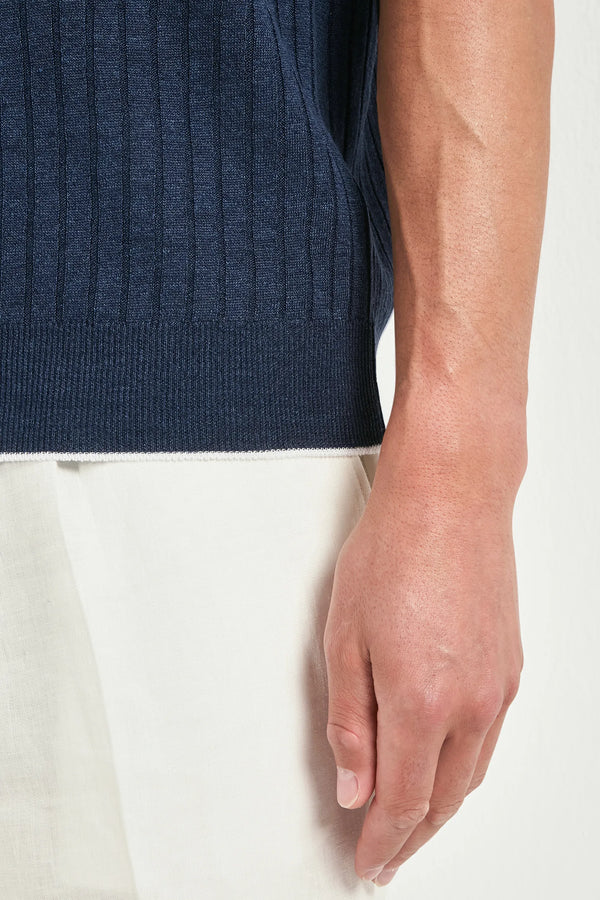 Close-up of a person wearing a navy blue sleeveless sweater and white pants on a white background