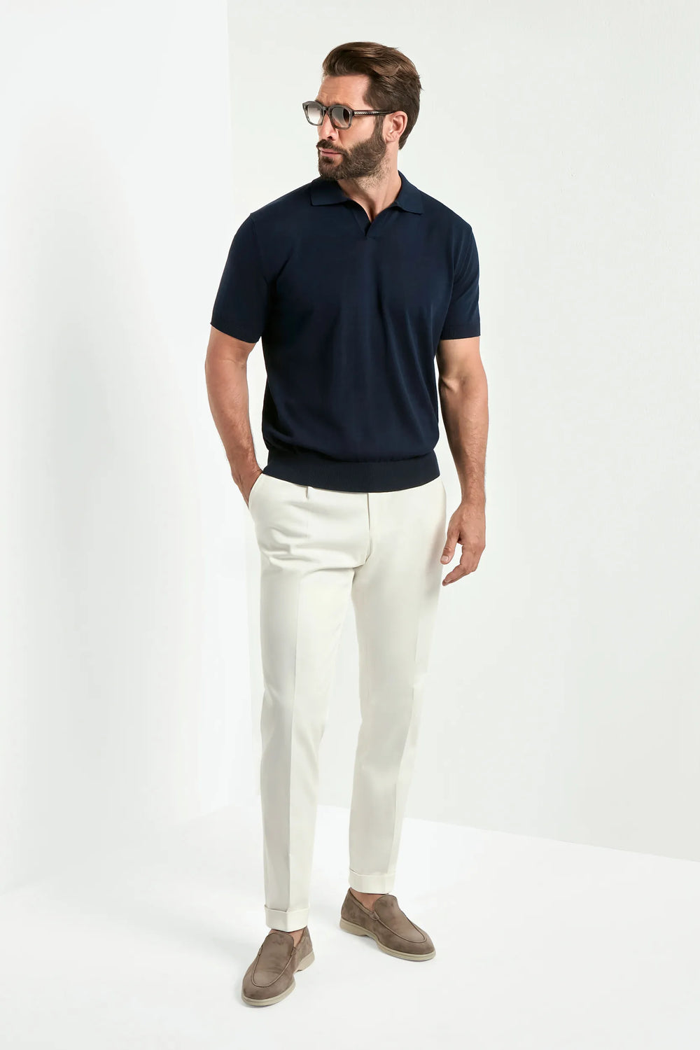 Man wearing a navy polo shirt and white pants on a white background