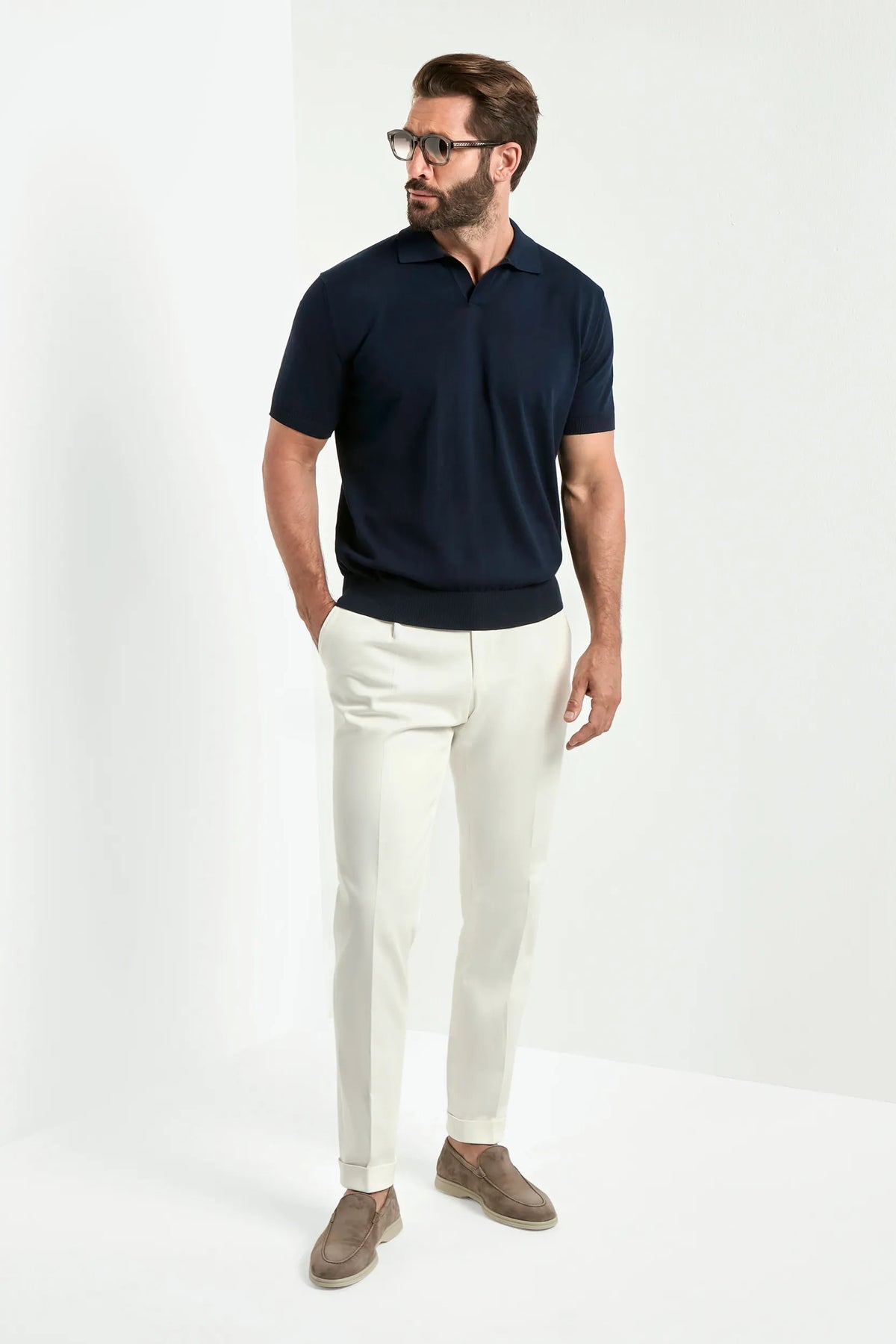 Man wearing a navy polo shirt and white pants on a white background
