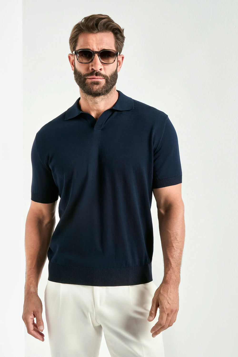 Man wearing a navy polo shirt and white pants against a white background