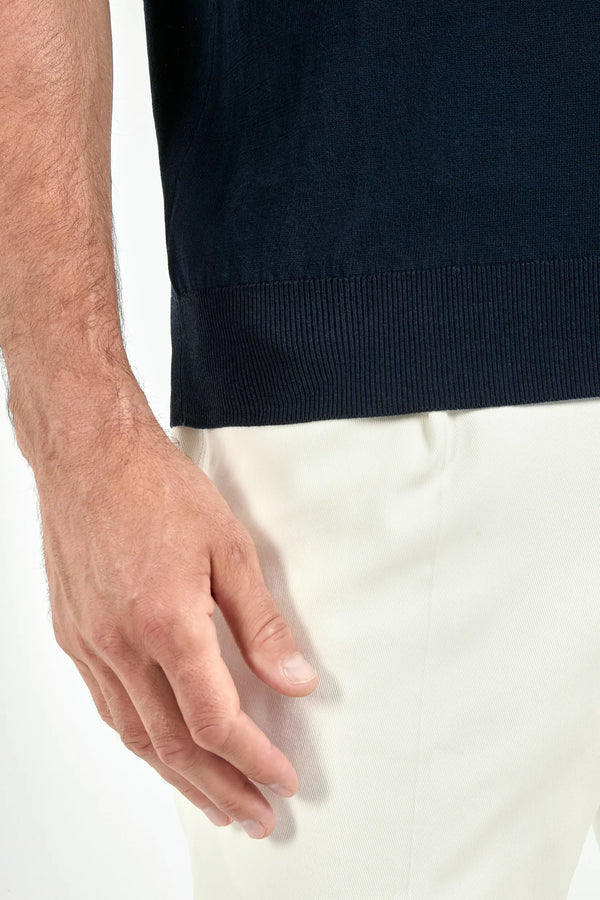 Close-up of a person wearing a navy sweater and white pants.