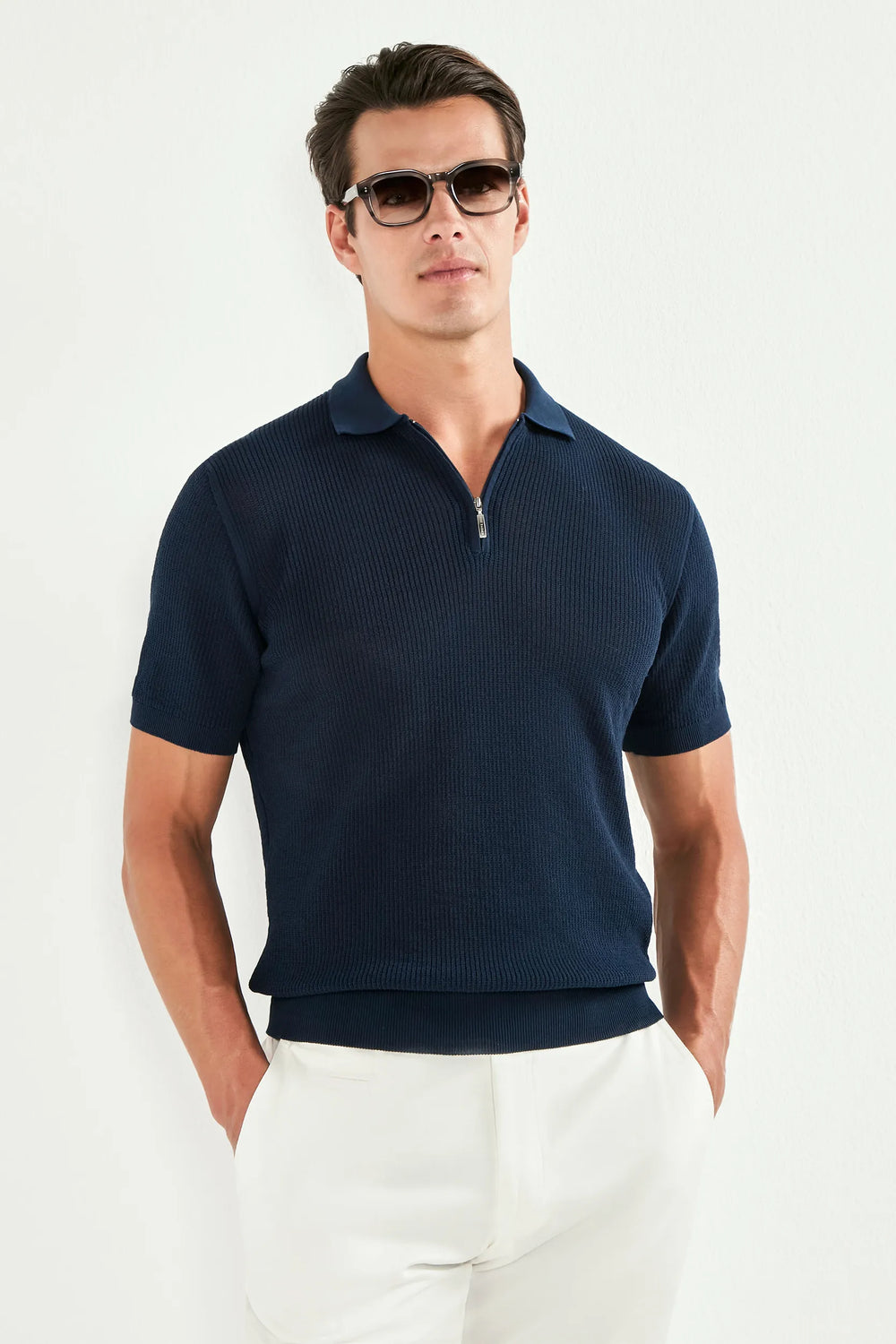 Man wearing a navy polo shirt and white pants against a white background