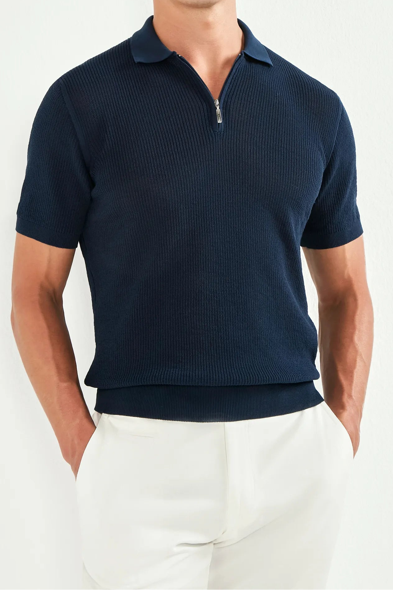 Man wearing a navy polo shirt and white pants against a white background