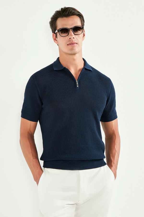 Man wearing a navy polo shirt and white pants against a white background