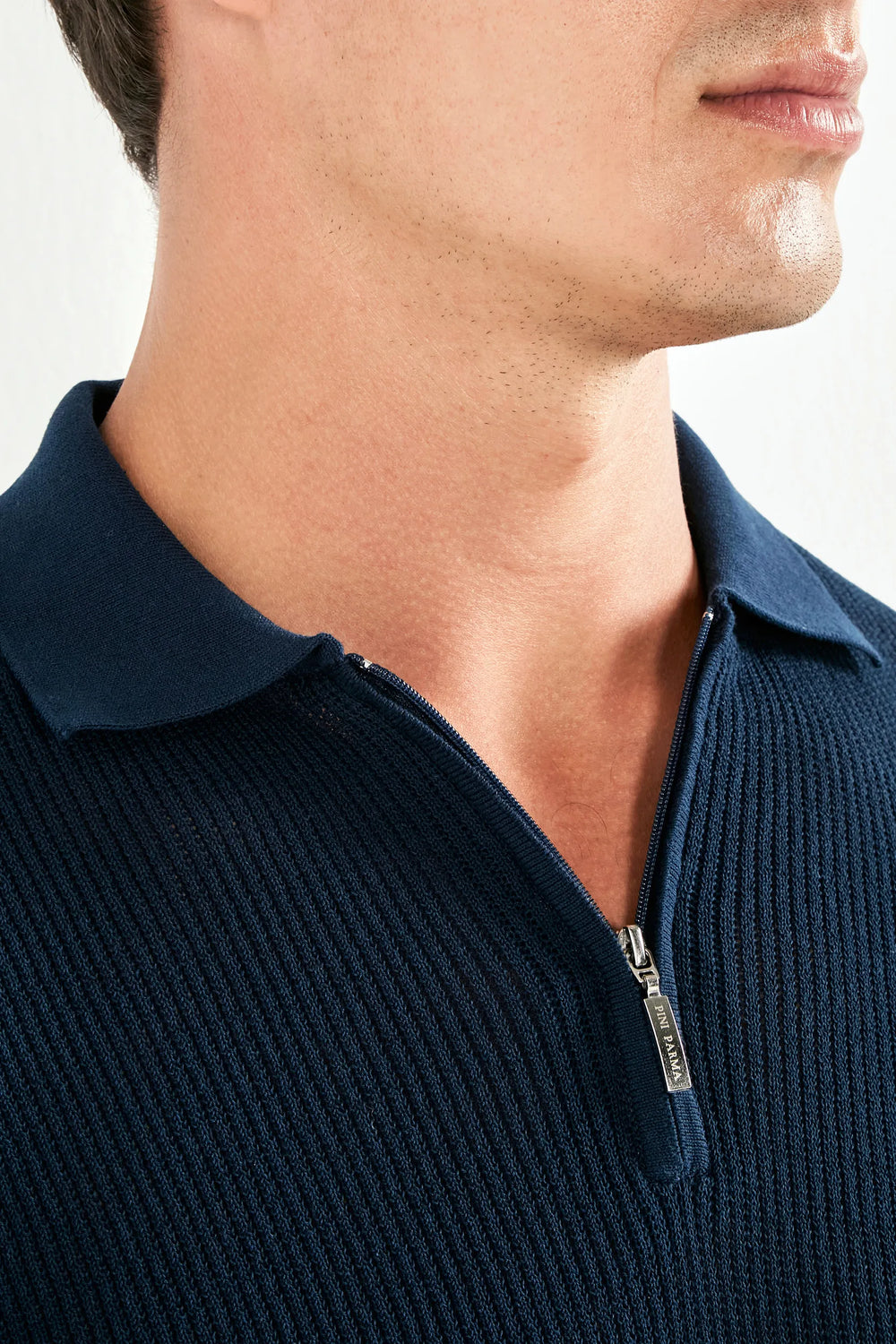 Close-up of a person wearing a navy blue ribbed sweater with a zipper.