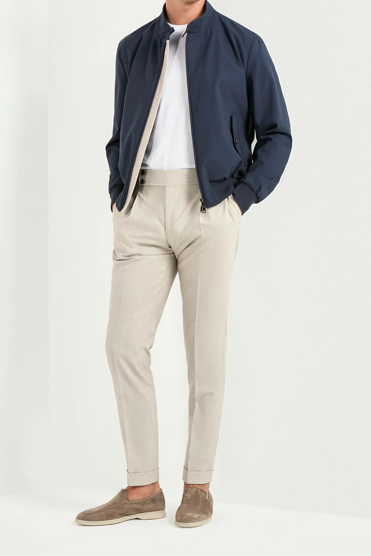 Man wearing a navy jacket, white shirt, beige pants, and brown shoes on a white background