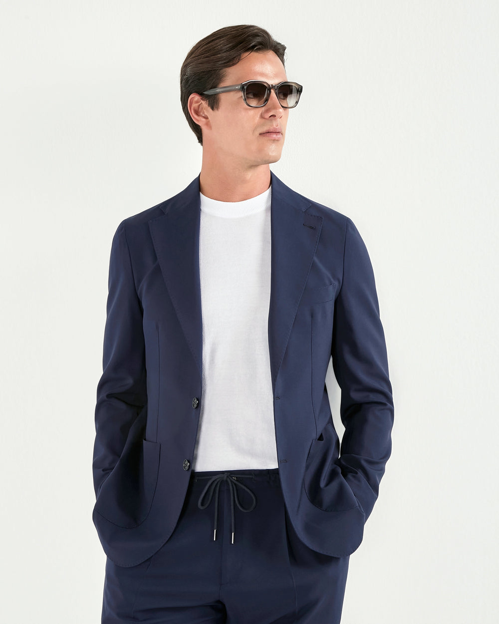Man wearing a navy blue suit with sunglasses on a light gray background
