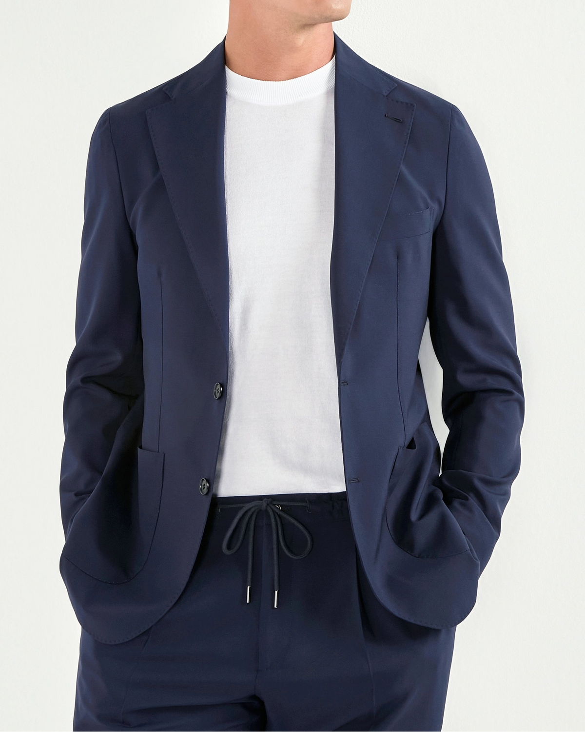 Man wearing a navy blue suit with sunglasses on a light gray background