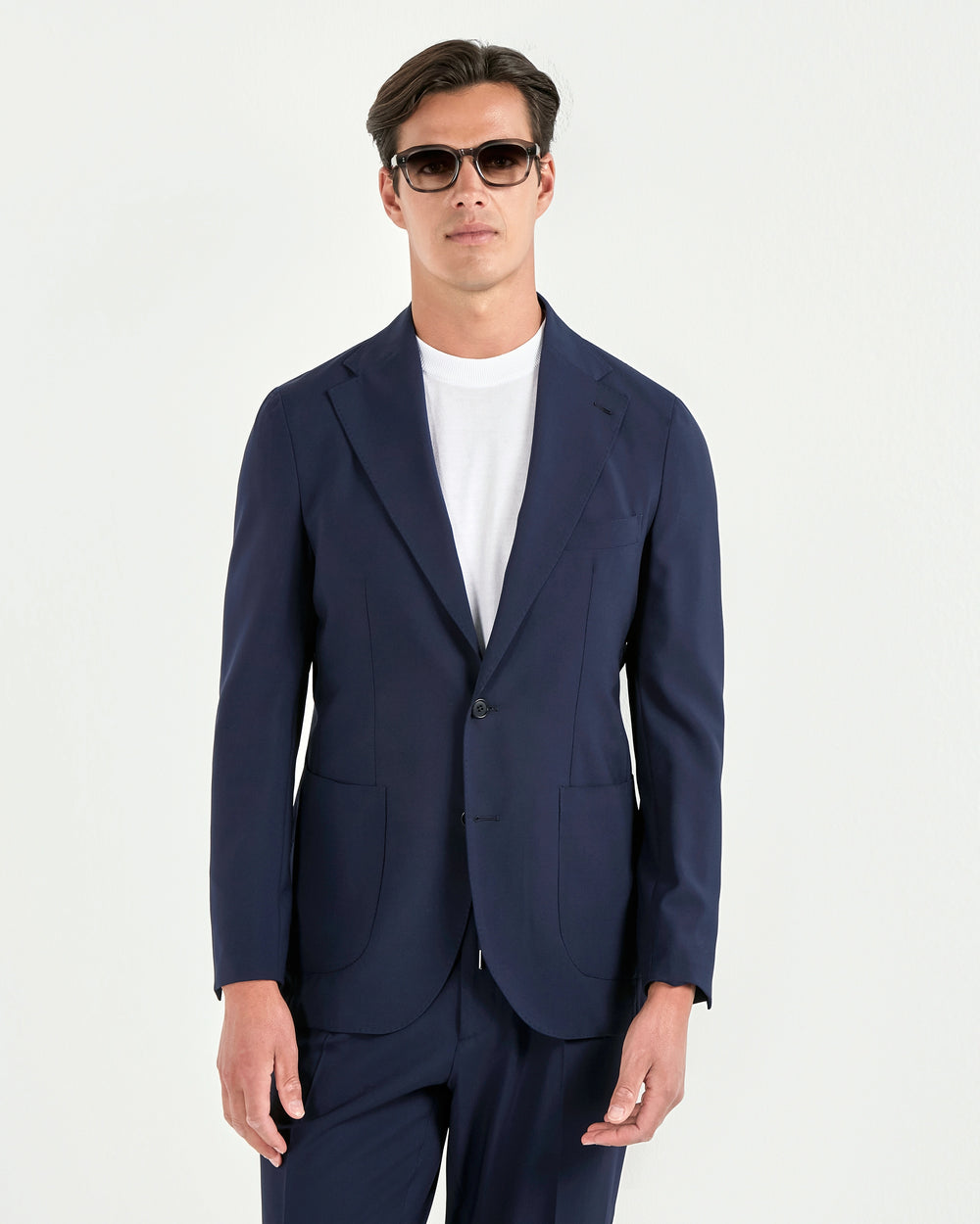 Man wearing a navy suit and sunglasses on a white background