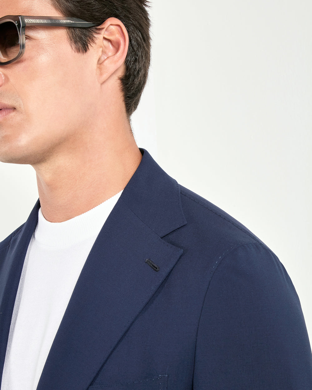 Man wearing a navy blazer over a white shirt with a neutral background