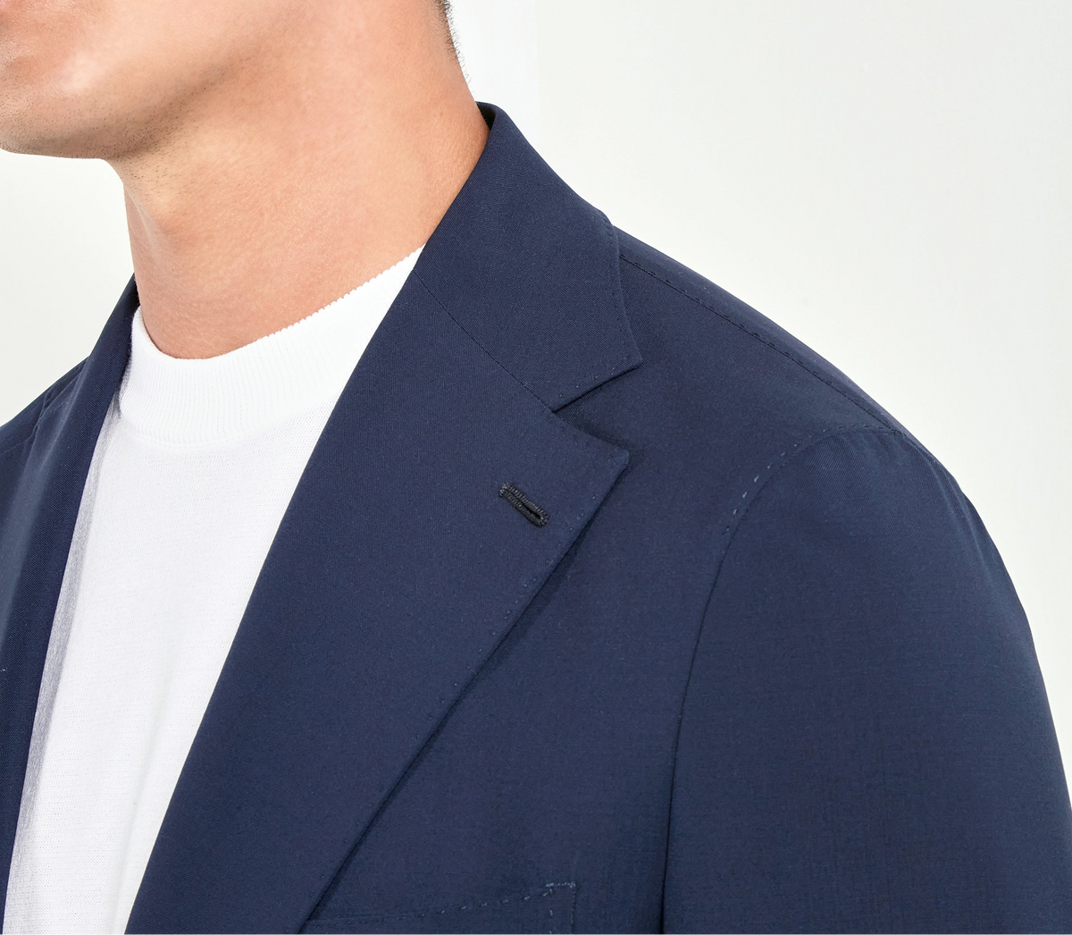Man wearing a navy blazer over a white shirt with a neutral background
