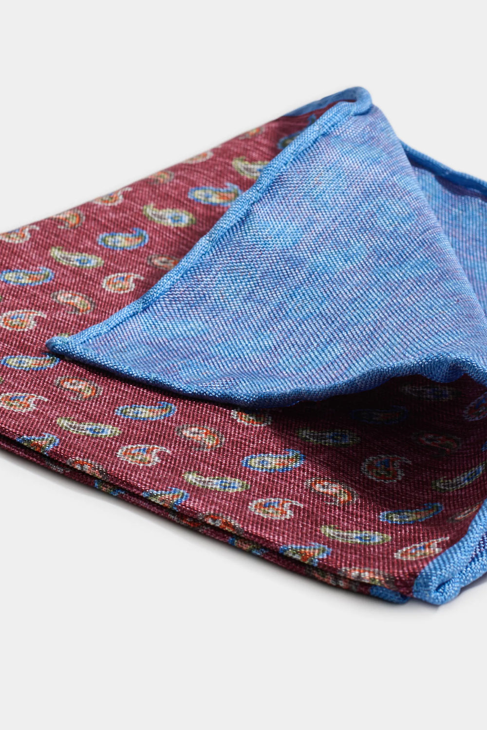 Folded fabric with paisley pattern on one side and blue textured fabric on the other, on a white background.