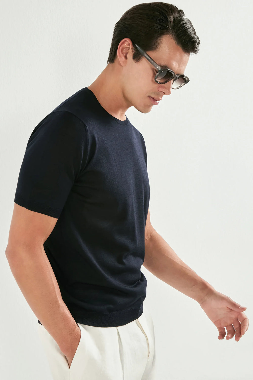 Man wearing a navy blue t-shirt and white pants against a plain background