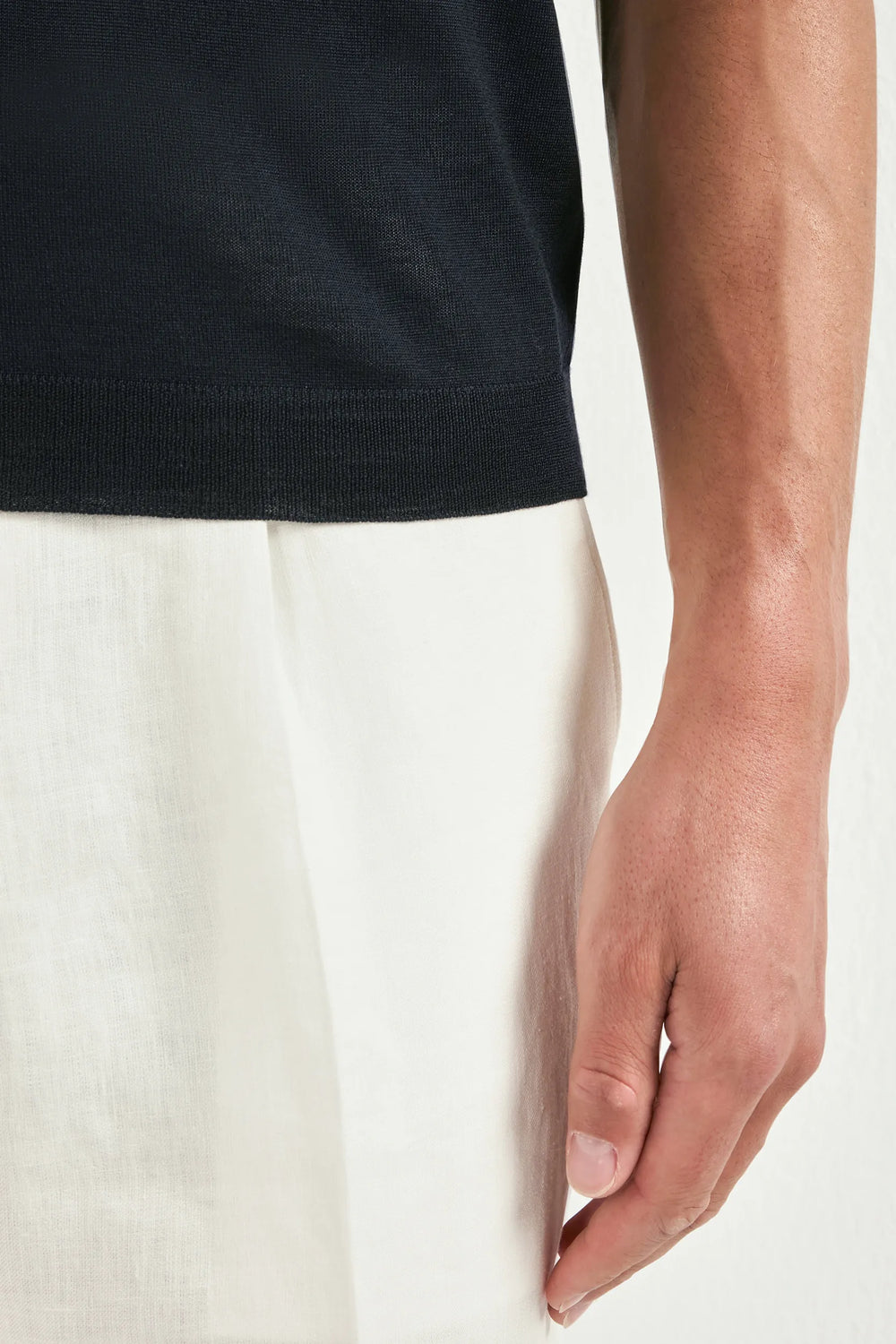 Close-up of a person wearing a black shirt and white pants on a plain background