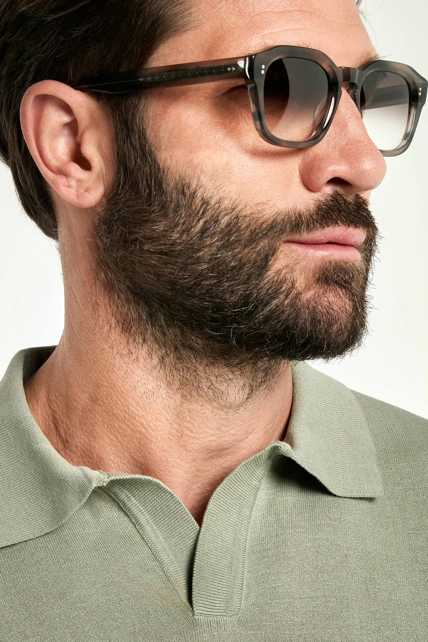 Close-up of a man wearing sunglasses and a green polo shirt against a white background