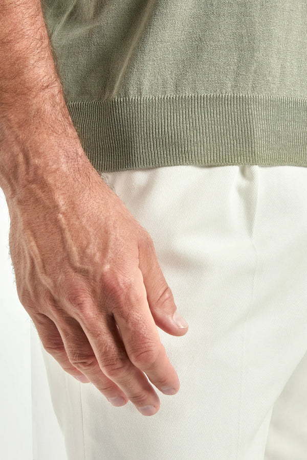 Close-up of a person wearing a green sweater and white pants.