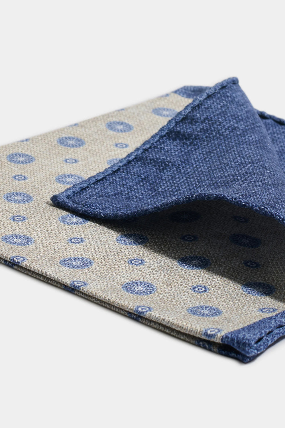 Two patterned cloths, one beige with blue circles and the other blue, on a light gray background.