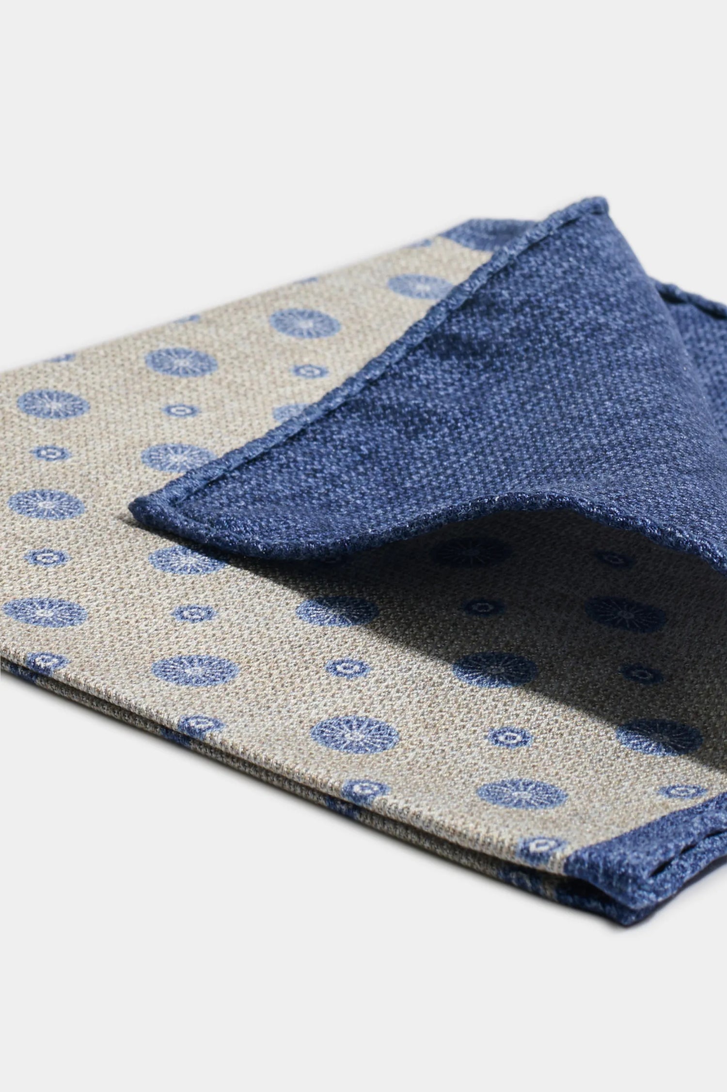 Two patterned cloths, one beige with blue circles and the other blue, on a light gray background.