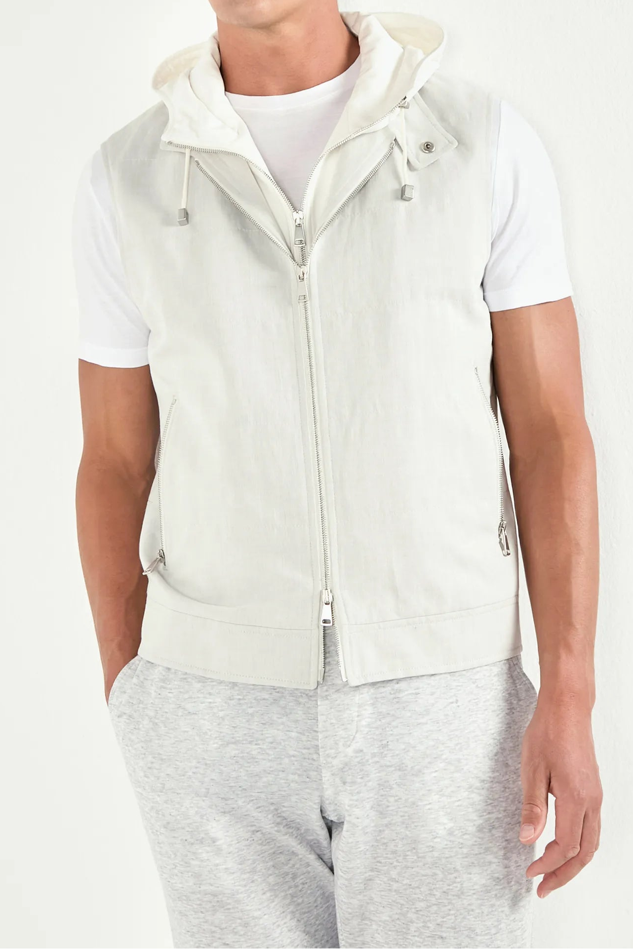 Man wearing a white vest over a white shirt with gray pants on a white background