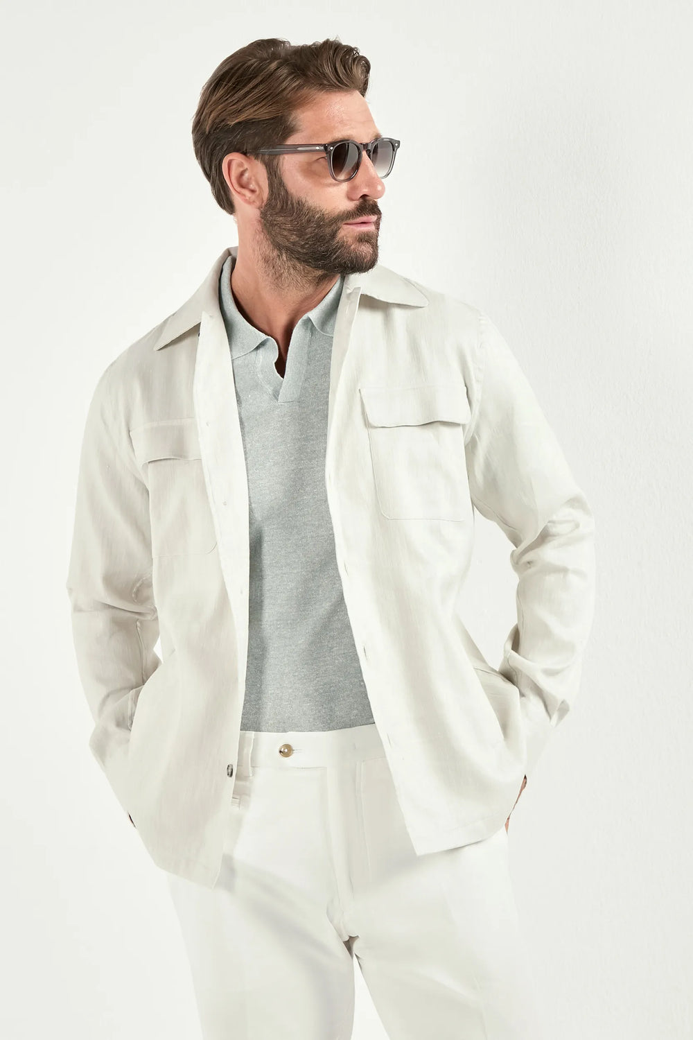 Person wearing a white jacket over a light green polo and white pants on a light background 