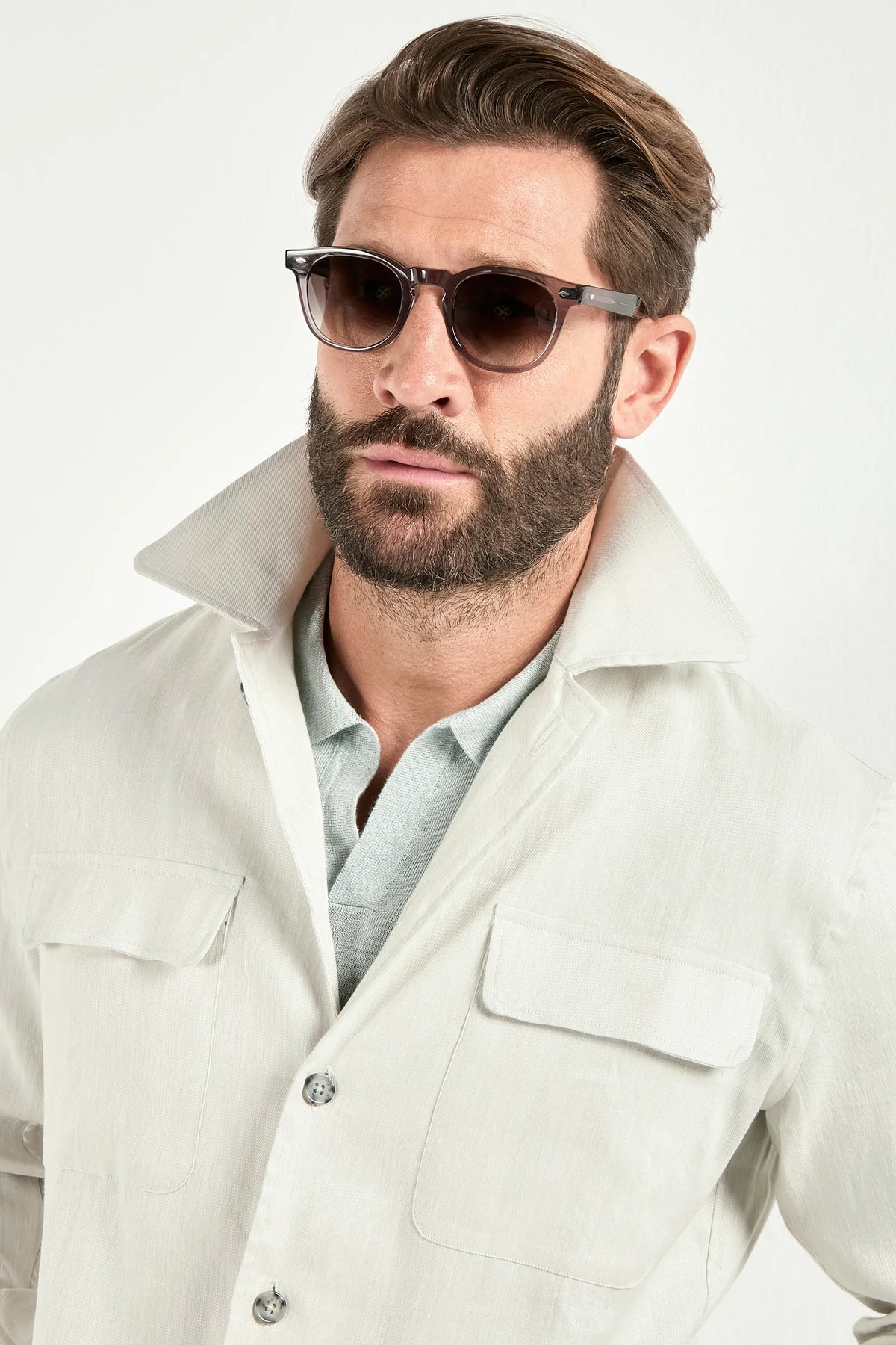 Person wearing a white jacket over a light green polo and white pants on a light background 
