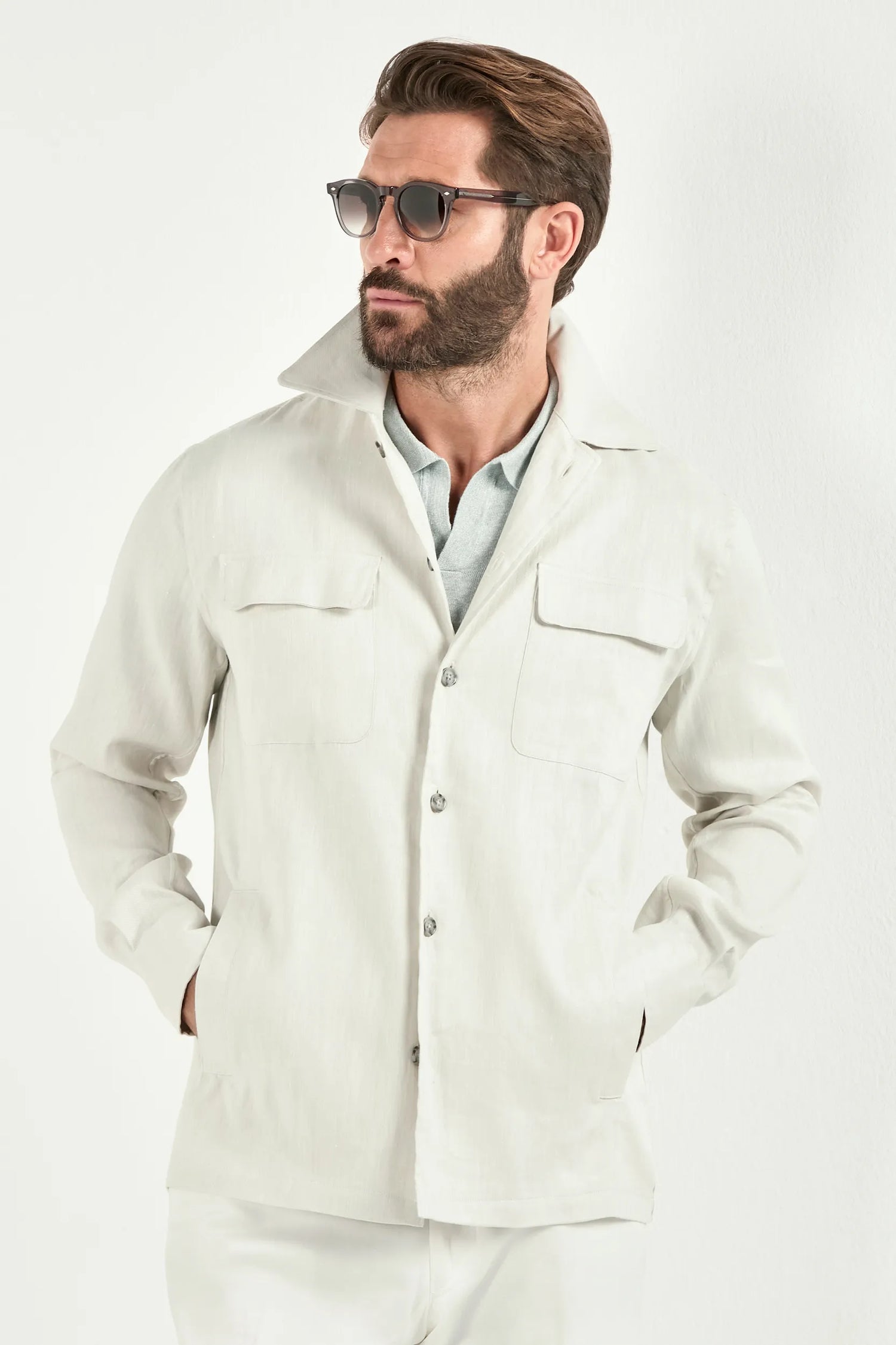 Person wearing a white jacket over a light green polo and white pants on a light background 