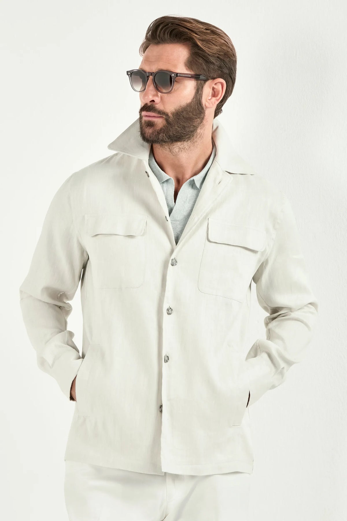 Person wearing a white jacket over a light green polo and white pants on a light background 
