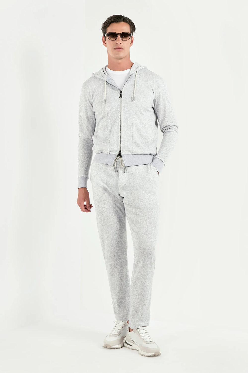 Man wearing a gray hoodie and pants with sunglasses on a white background