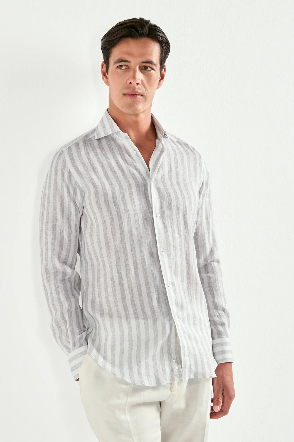 Man wearing a striped shirt and white pants on a plain background