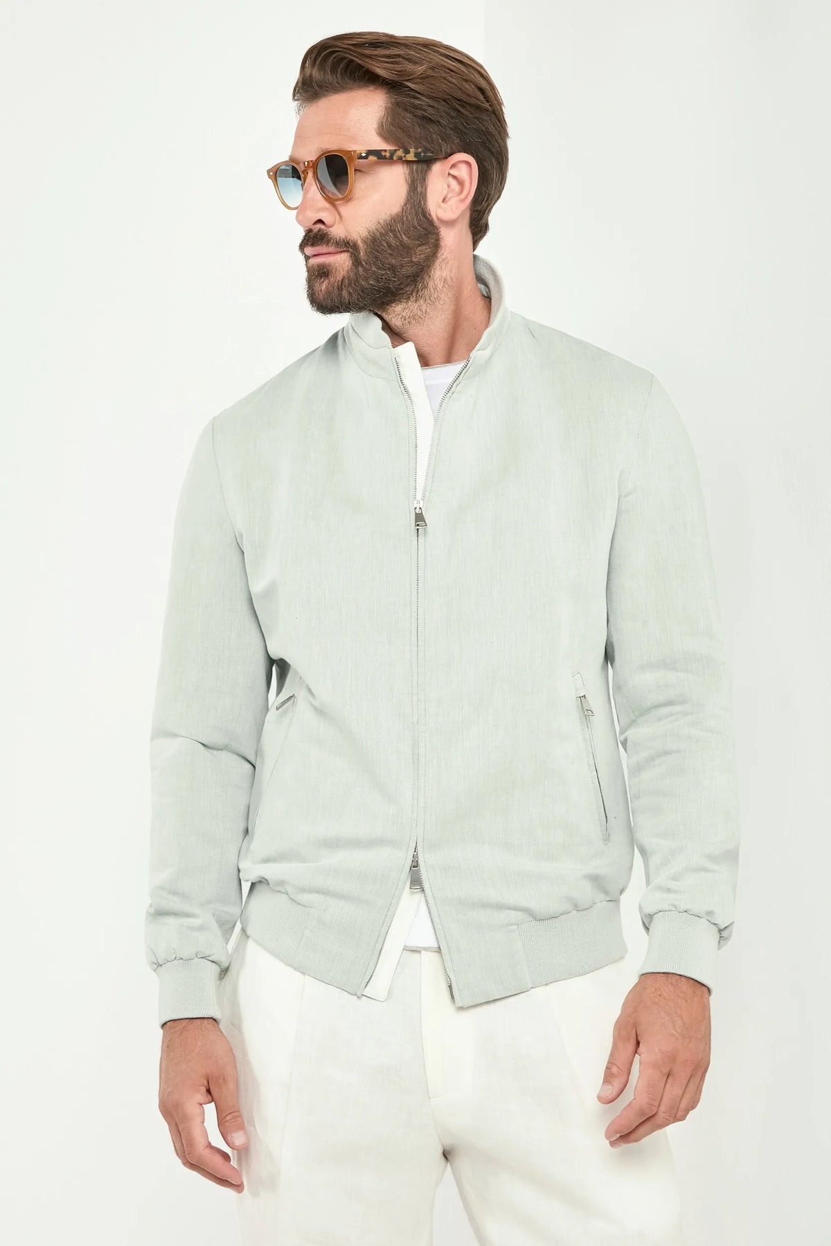 Man wearing a light green bomber jacket and white pants on a white background