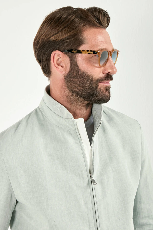 Man wearing a light green jacket and sunglasses on a white background