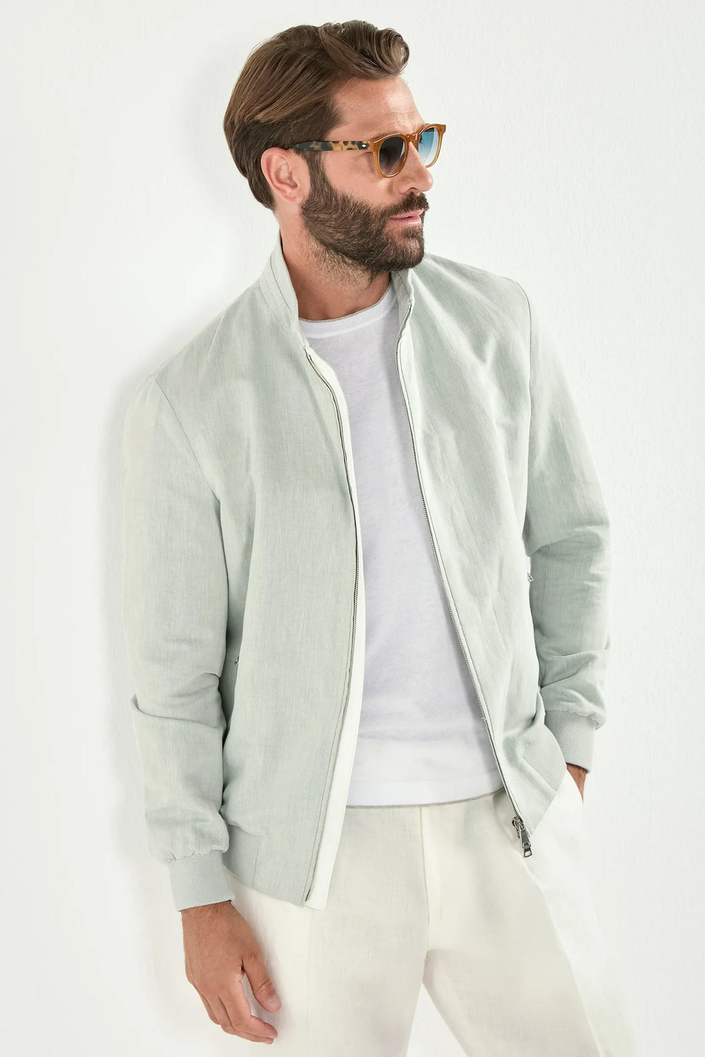 Man wearing a light green jacket over a white shirt and pants on a white background