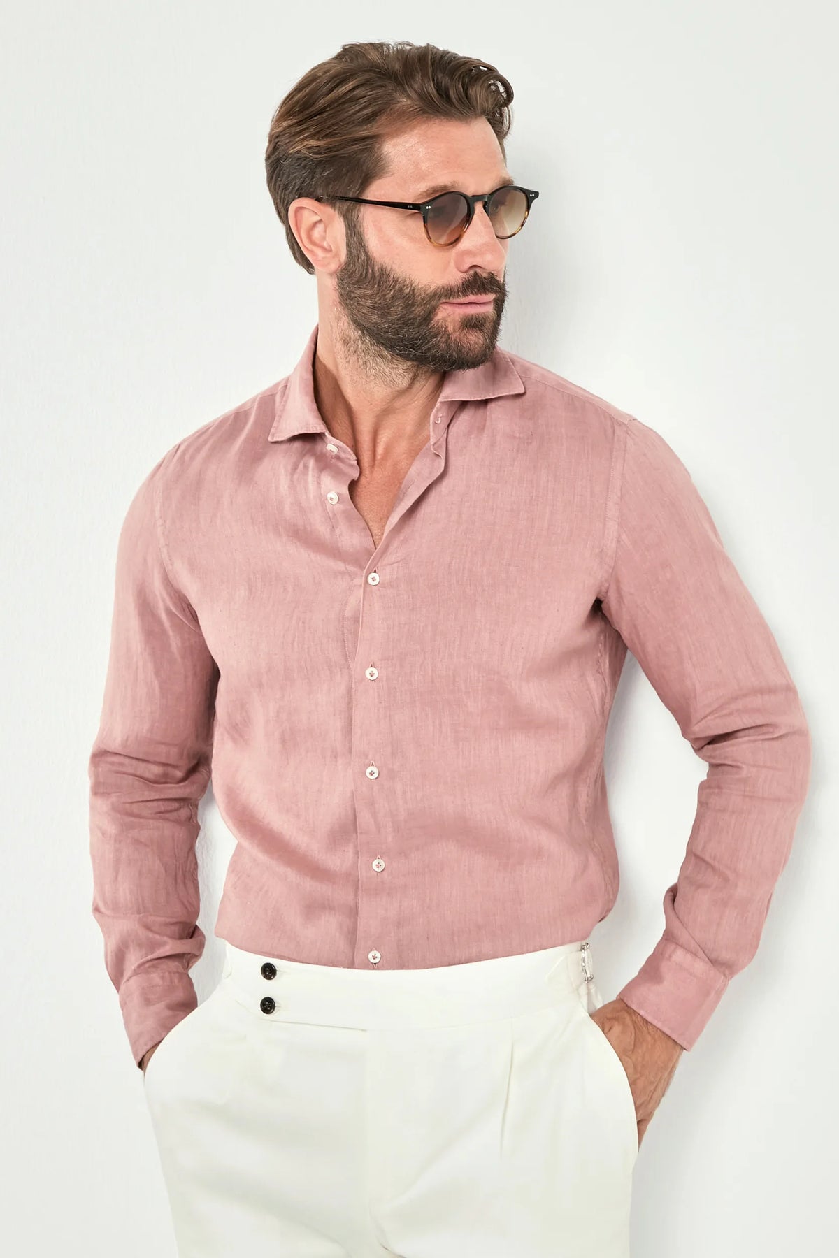 Man wearing a pink shirt and white pants against a light background