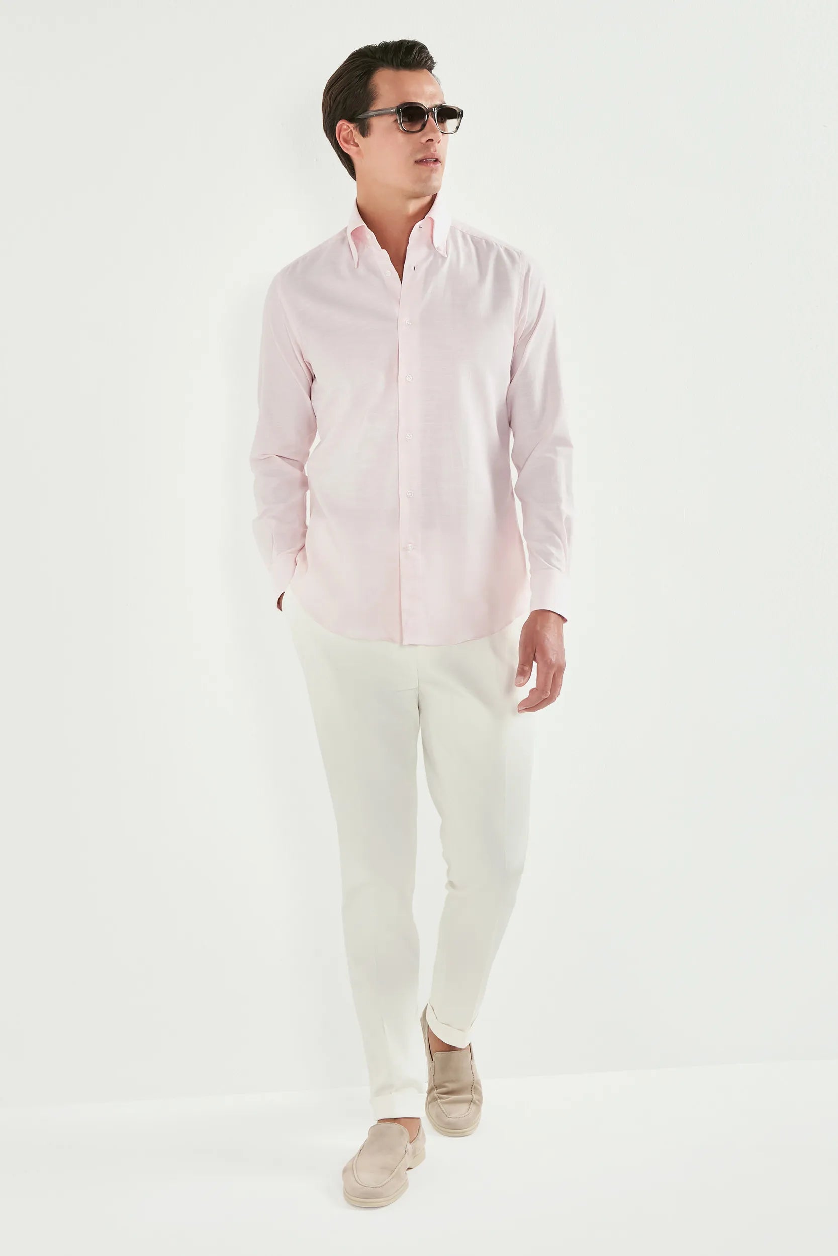 Man wearing a light pink shirt and white pants on a white background