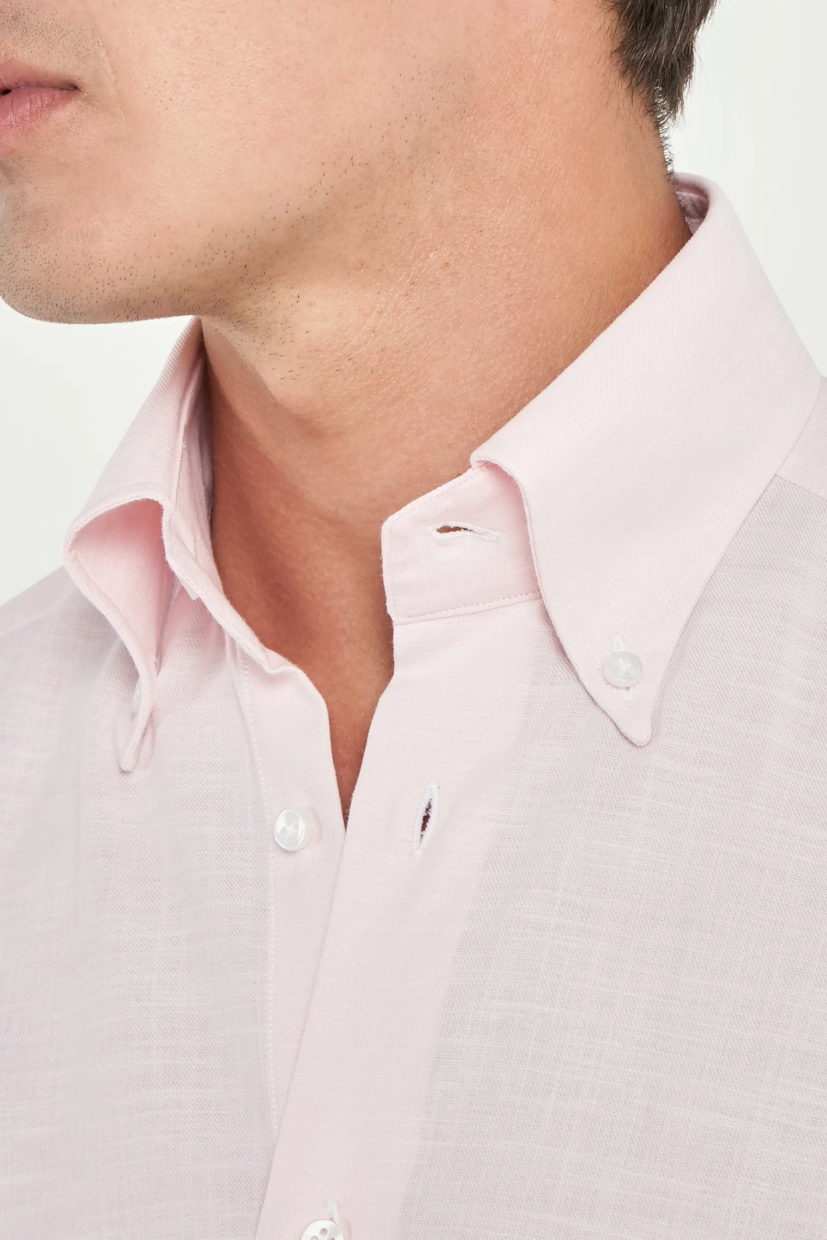 Close-up of a man wearing a light pink shirt with a collar.