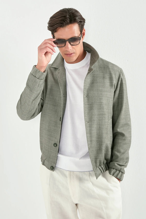 Person wearing a white t-shirt under a sage bomber jaket and white pants on a light background 