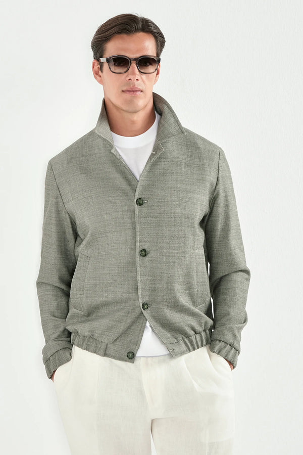 Person wearing a white t-shirt under a sage bomber jaket and white pants on a light background 