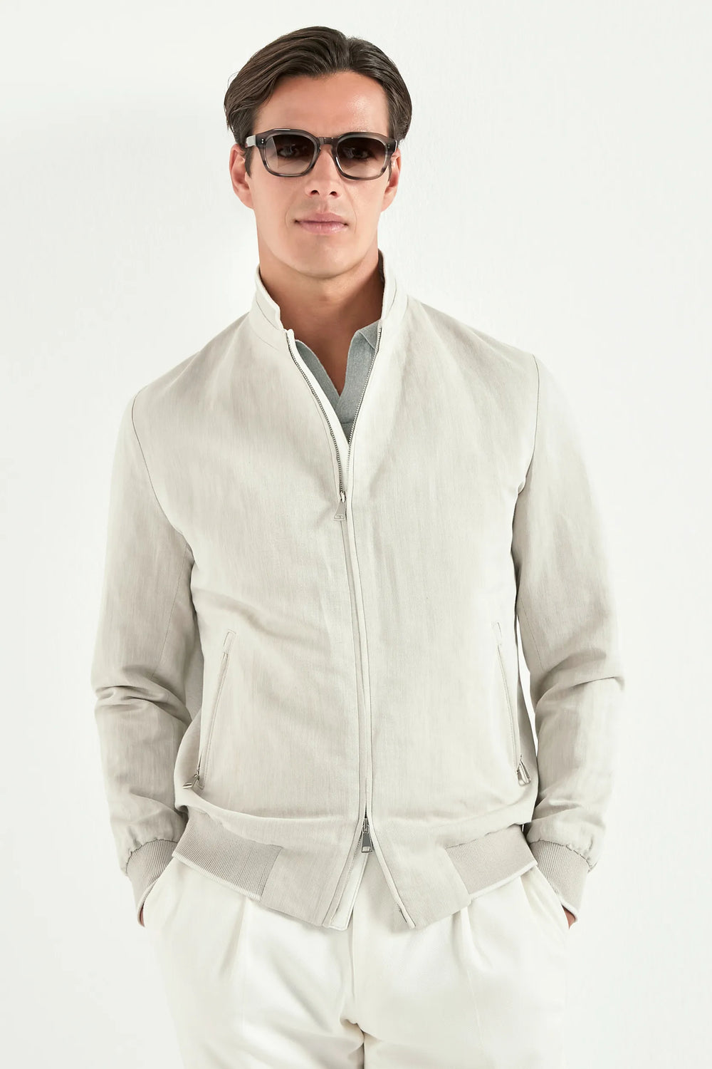 Man wearing a light gray zip-up jacket over a white shirt with sunglasses on a white background