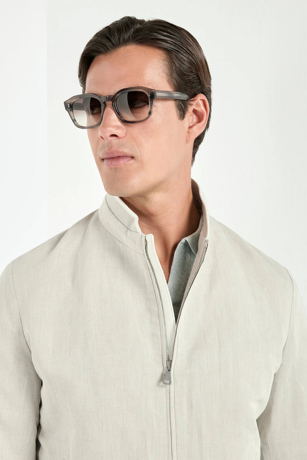 Man wearing sunglasses and a light-colored jacket on a white background