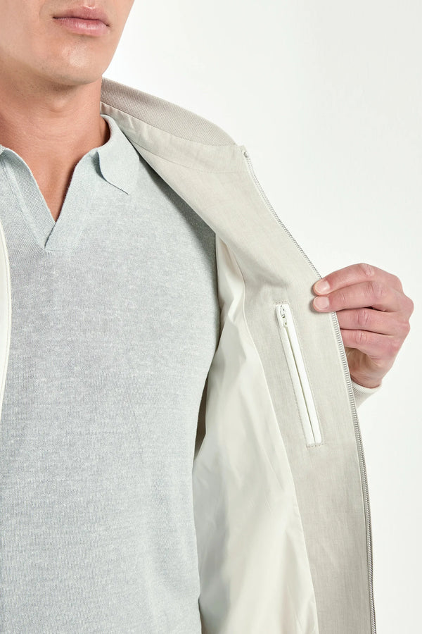 Person wearing a light gray jacket with a white zipper on a plain background